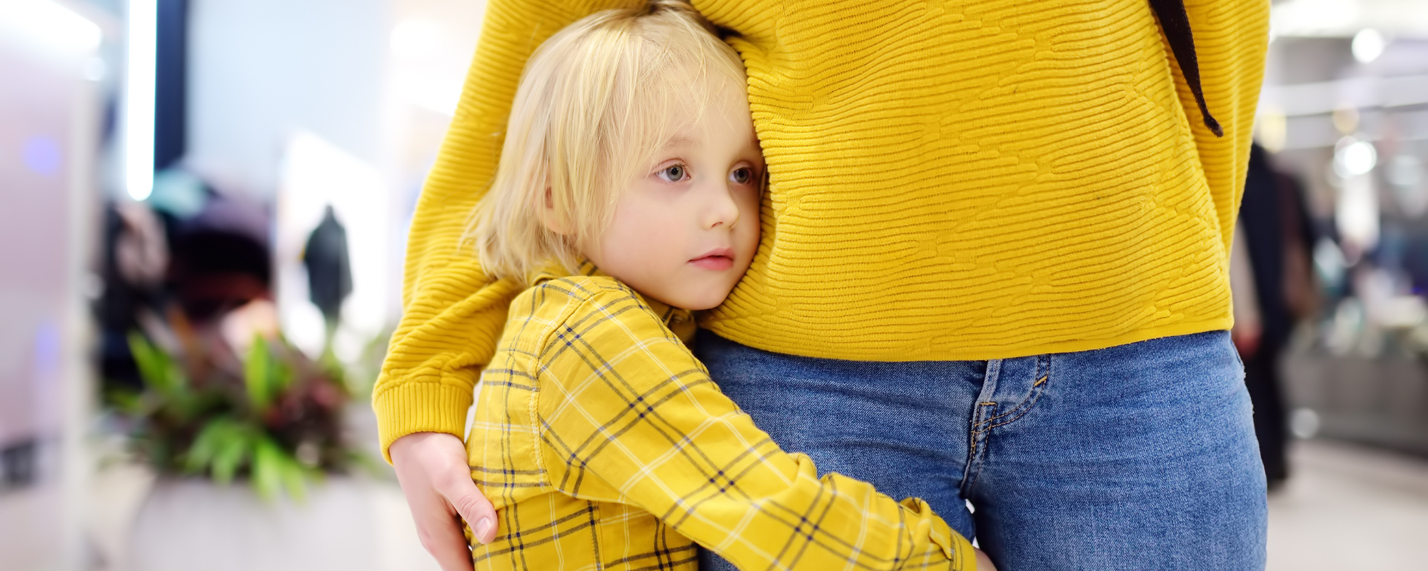 photo of a blond child in a yellow shirt hugging their grownup, also wearing a yellow shirt. The child looks anxious and like they don't want to let go of their grown up.