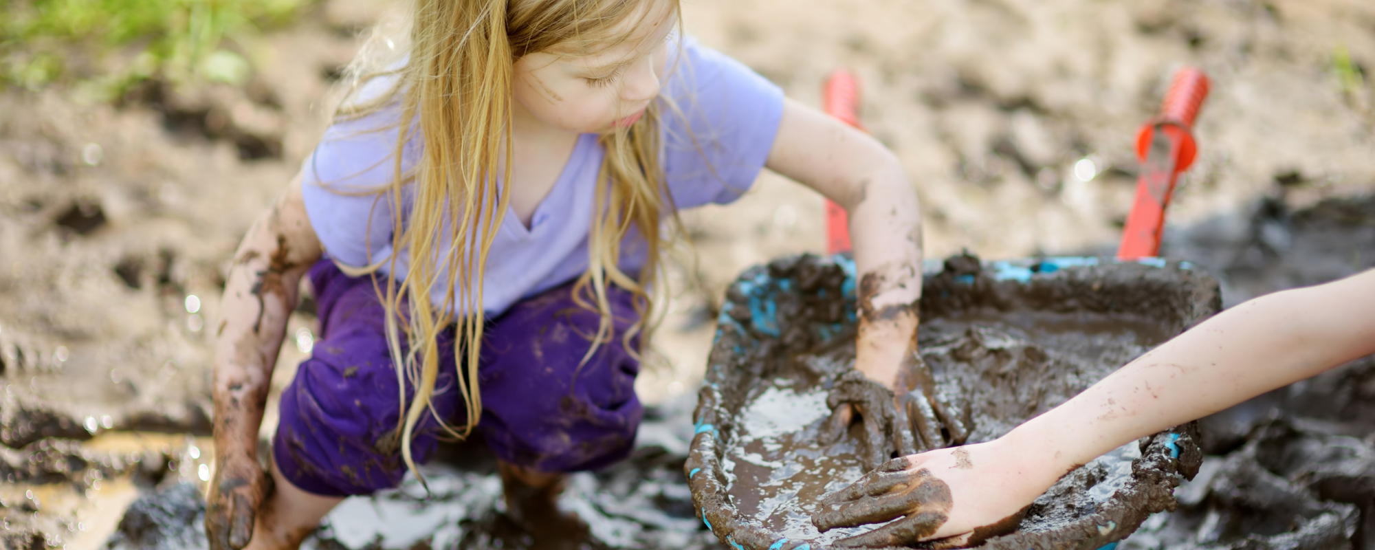 preschooler playing outside with a bucket of mud