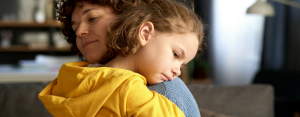sad child hugging an adult who looks calm and safe.