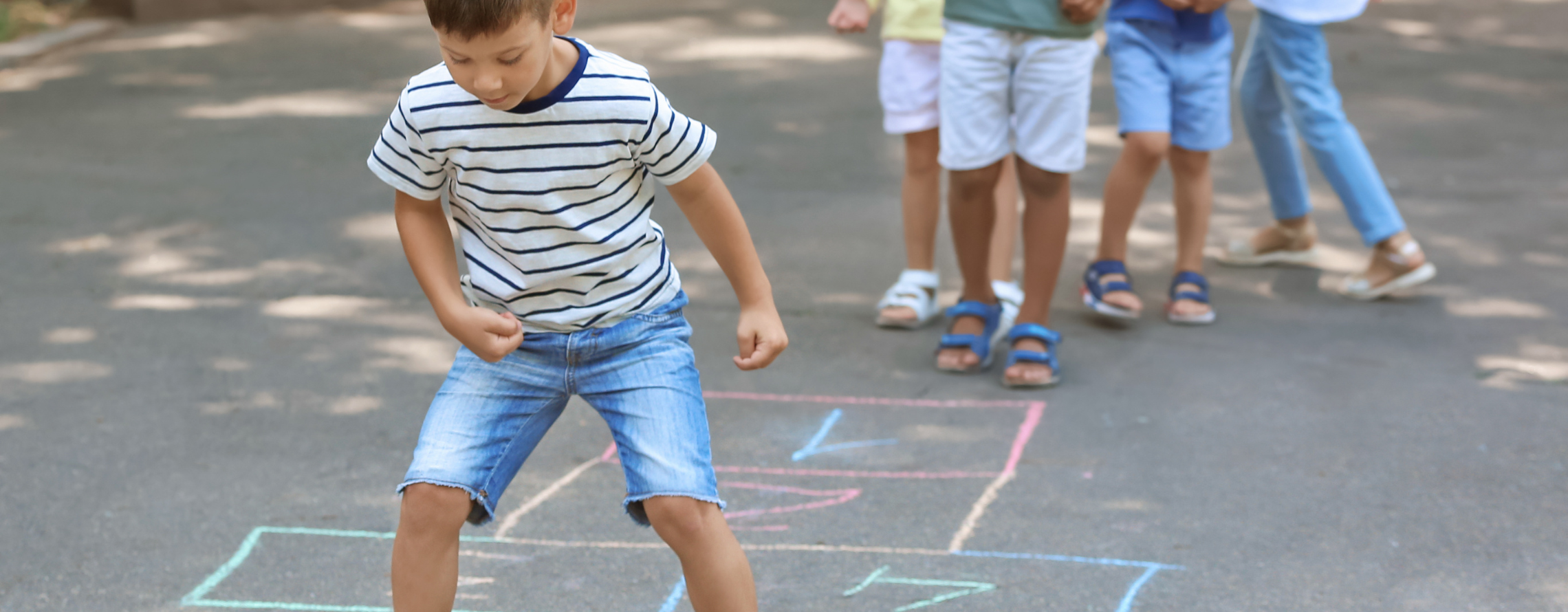 boy playing hopscotch with four other children waiting in line to play too
